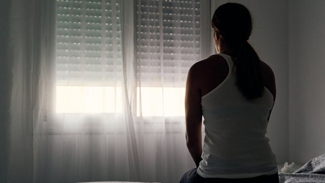 Mujer sentada en una cama mirando por la ventana