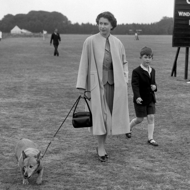 Королева Елизавета II гуляет по Виндзорскому парку с принцем Чарльзом, наблюдая, как герцог Эдинбургский играет в поло