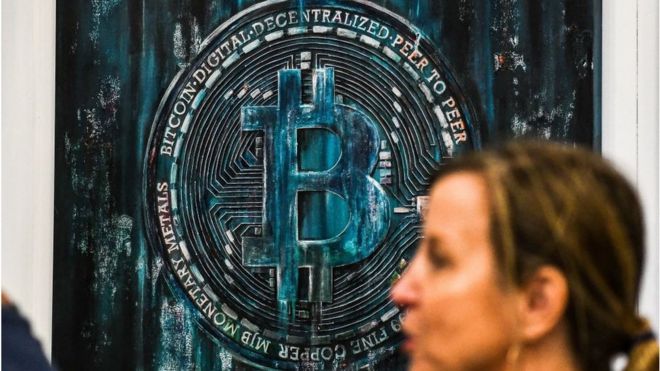Una mujer camina al frente de una instalación de arte inspirada en Bitcoin durante la conferencia 2022 celebrada en Miami Beach