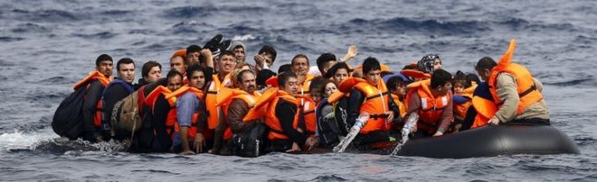 Сирийские беженцы призывают к помощи и сливают воду со своего затопляющего плота, когда они приближаются к греческому острову Лесбос