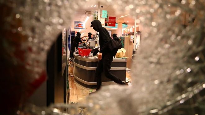 A protester is seen through smashed glass looting what appears to be a supermarket in Hamburg