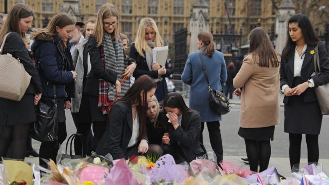 Люди смотрят на цветочные дани, оставленные жертвам нападения