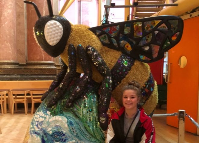 Амелия Томпсон сидит у скульптуры пчелы