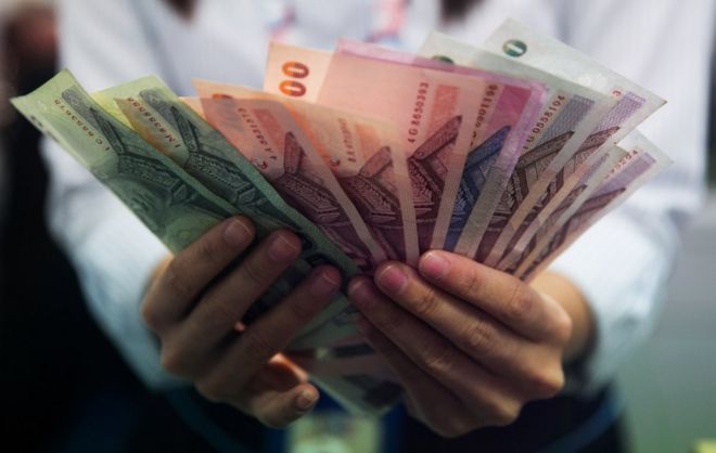 A money exchange bank teller counts Thai baht in Bangkok, Thailand.