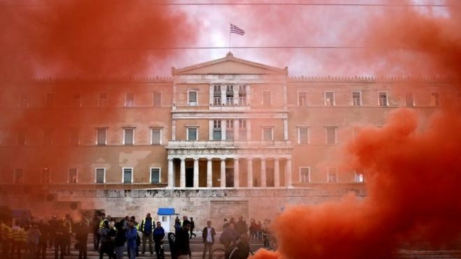 Здание парламента видно сквозь факельный дым во время демонстрации офицеров в форме, отмечающих 24-часовую всеобщую забастовку против последнего раунда жесткой экономии в Афинах (17 мая 2017 года)