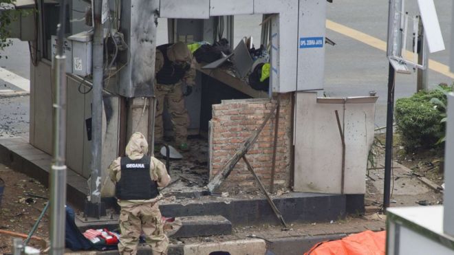 Два индонезийских полицейских осматривают бомбы, поврежденные на постах ГАИ возле поврежденной кофейни Starbucks после серии взрывов, произошедших в центральной части Джакарты 14 января 2016 года