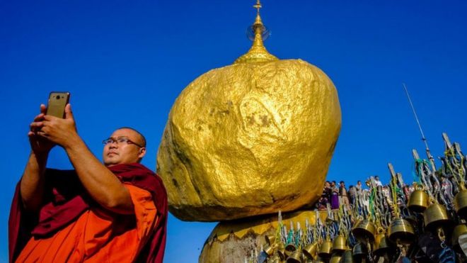 Буддийский монах делает селфи перед золотой скалой