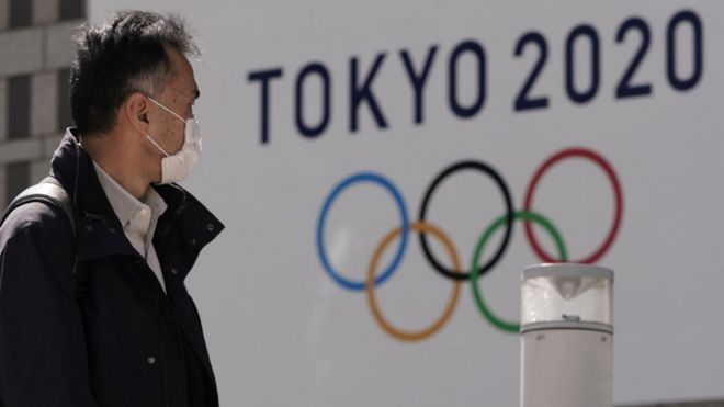 A pedestrian wearing a mask walks past the emblem of Tokyo 2020 Olympics in Tokyo.