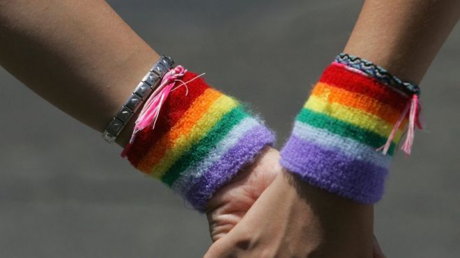 Лесбийская пара в радужных браслетах держатся за руки