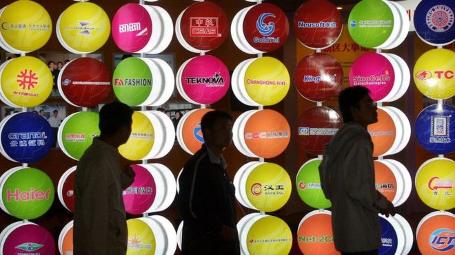 Customers walk past signs for companies in China.