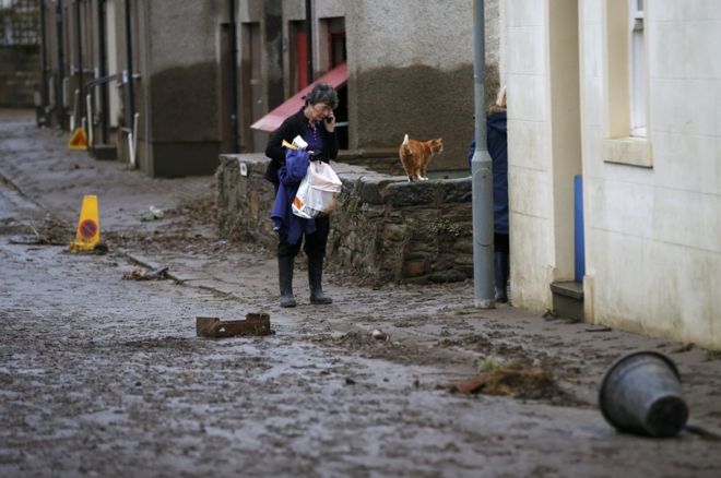 Женщина идет по улице, покрытой грязью и мусором после того, как в Кокермуте затонуло наводнение