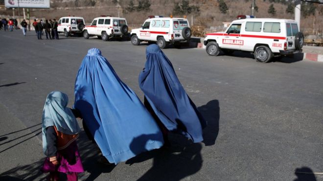 Афганские женщины проходят мимо машин скорой помощи на месте обстрела гостиницы в Кабуле 21 января 2018 года