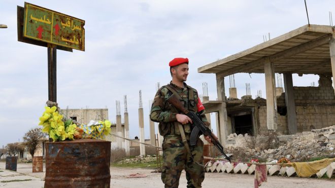 جندي سوري يقف الى جانب لافتة طريق تشير الى إدلب وسراقب وحلب