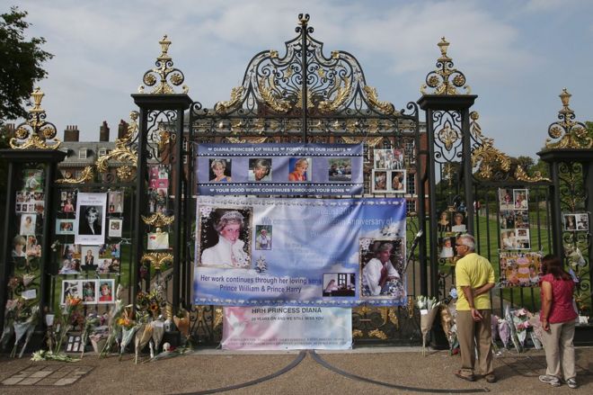 Посетители смотрят фотографии Дианы, принцессы Уэльской, и цветочные подношения, оставленные возле Кенсингтонского дворца в центральном Лондоне 29 августа 2017 года