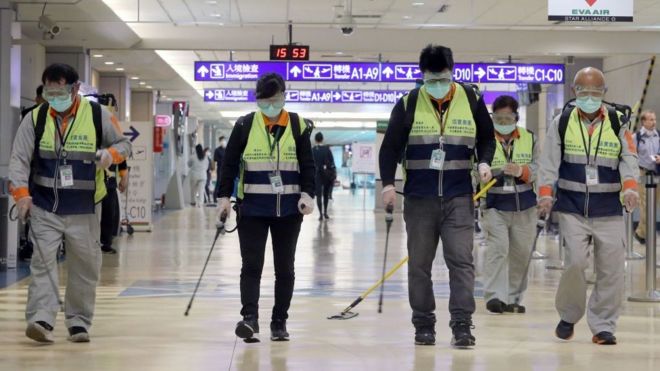 Masked workers disinfect a passenger throughfare at the Taoyuan International Airport on January 22, 2020