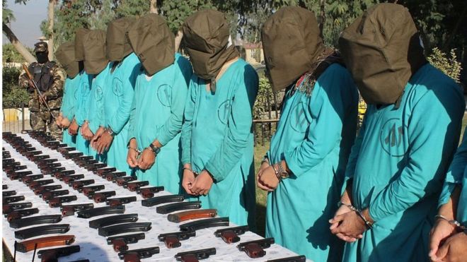 Предполагаемые члены ИГ и талибов в капюшонах, стоящие перед столом с оружием в Джалал-Абаде на востоке Афганистана 6 декабря 2016 года.