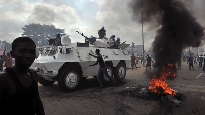 Миротворцы ООН проезжают мимо сторонников Алассана Уаттара, когда они демонстрируют и сжигают шины в районе Абобо в Абиджане 19 февраля 2011 года