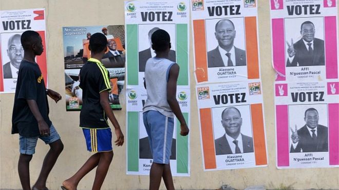 14 октября 2015 года в Кокоди-Абиджане мальчики проходят мимо плакатов кампании кандидатов в президенты на выборах в Кот-д'Ивуар.