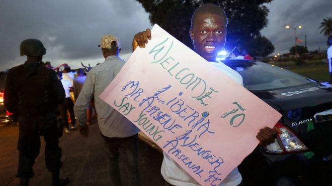 Поклонник «Арсенала» держит плакат с приветствием бывшего футбольного тренера Арсена Венгера по прибытии в международный аэропорт Робертс в Харбеле, Либерия, 22 августа 2018 года.