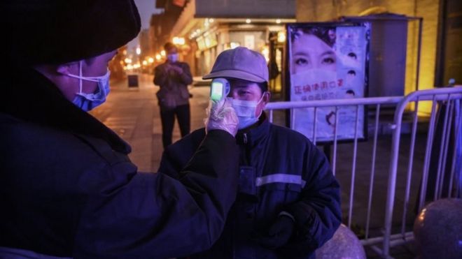 A Chinese worker wears a protective mask as she has her temperature checked on a nearly empty commercial area on February 12, 2020 in Beijing, China.