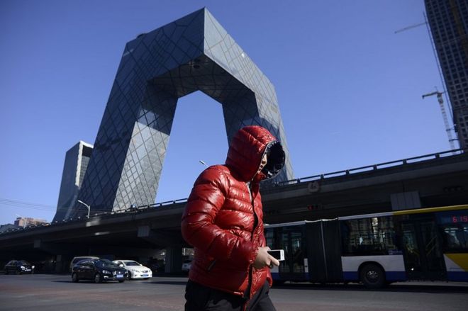 Мужчина идет по улице, когда на заднем плане 20 января 2017 года в центральном деловом районе Пекина маячит Башня видеонаблюдения.