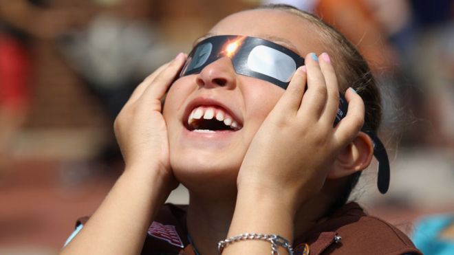 Imagem mostra menina usando óculos especiais para observar eclipse do sol