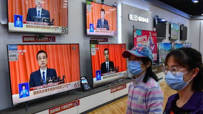 Shoppers walking past a broadcast of Chinese Premier Li Keqiang delivering his speech at the opening of the NPC