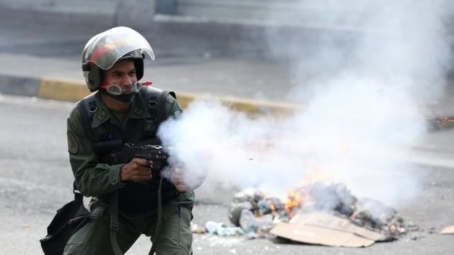 Сотрудник ОМОНа стреляет слезоточивым газом во время столкновения с демонстрантами во время митинга в Каракасе, Венесуэла, 8 апреля 2017 года