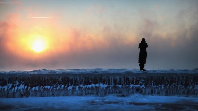 Hombre parado sobre un bloque de hielo frente al Sol.