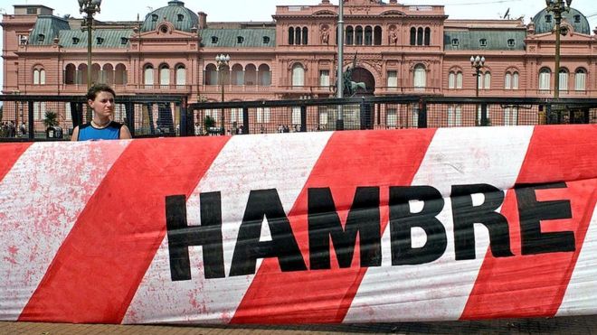 Un joven con un cartel que se lee "hambre" con la Casa Rosada de fondo.