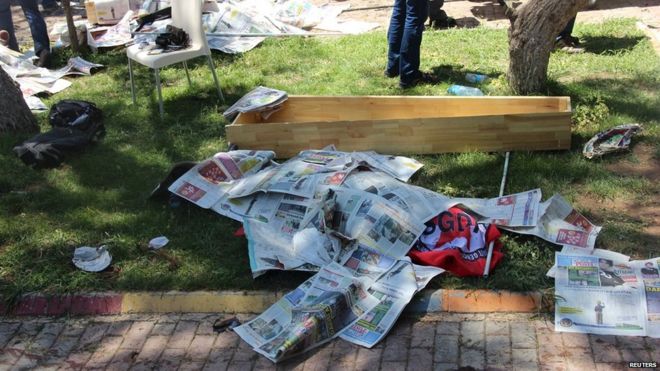 Тело жертвы, покрытое газетами, лежит рядом с гробом после взрыва в Суруке, Турция (20 июля 2015 года)