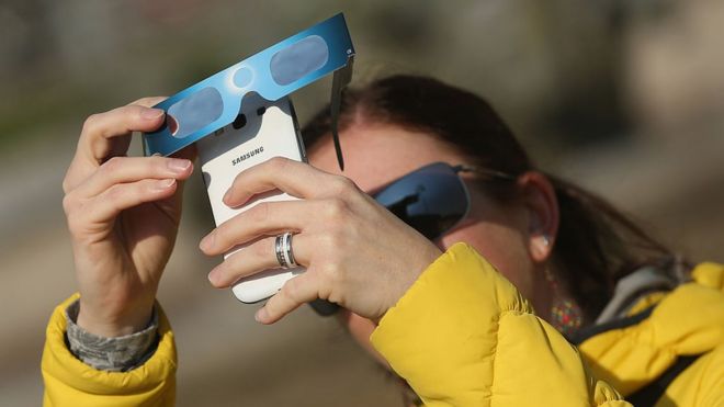 Mujer sacando foto al eclipse con su celular.