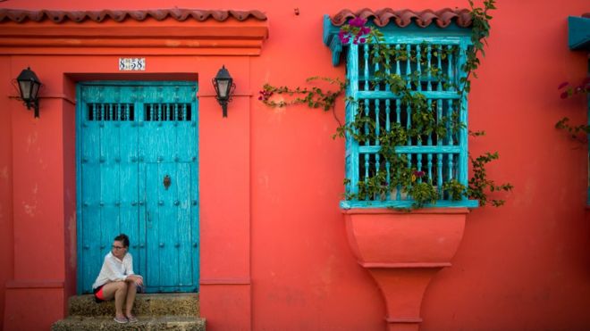 Una mujer está sentada en una escalera en la fachada de una casa colonial del casco colonial de Cartagena de Indias.