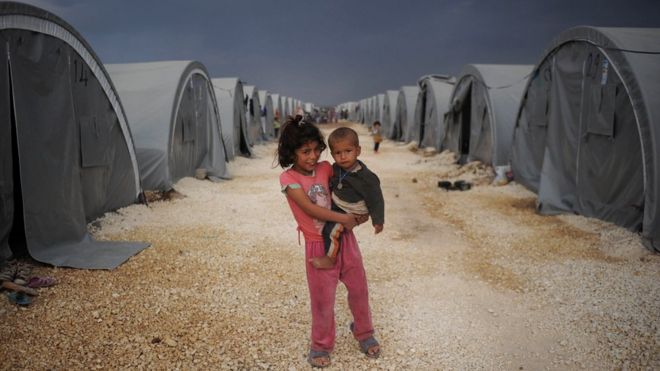Дети курдских беженцев, стоящие среди палаток в лагере беженцев в Турции