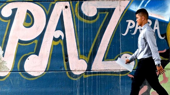 Un hombre pasa frente a un mural con la palabra paz en Colombia