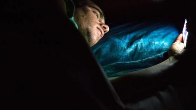 Hombre mirando su celular en la cama