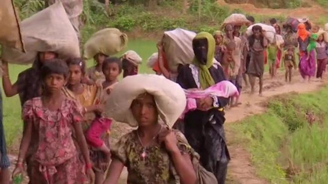 Refugiados rohingyas caminan en fila cargados con paquetes.