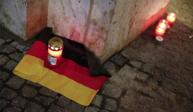 Свеча горит на немецком государственном флаге возле места, где грузовик пробивал толпу на рождественской ярмарке в Берлине