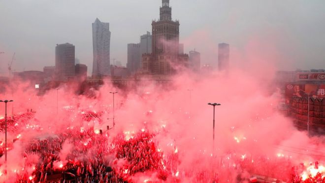 Люди несут польские флаги и флаеры, когда поют гимн Польши во время марша, посвященного 100-летию независимости Польши, в Варшаве, 11 ноября 2018 года