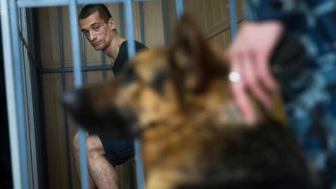 Русский художник Петр Павленский смотрит на полицейскую собаку, сидя в клетке в зале суда в Москве, Россия, среда, 8 июня 2016 г.