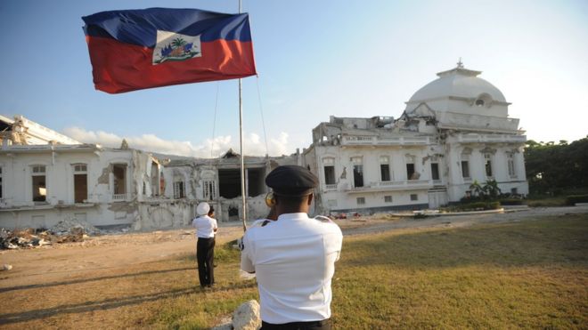 Президентские охранники Гаити опускают гаитянский флаг 19 апреля 2011 года перед разрушенным президентским дворцом в Порт-о-Пренсе