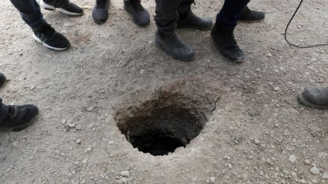 Police officers and journalists gather around the exit of a tunnel allegedly used to escape from Gilboa Prison, northern Israel (6 September 2021)