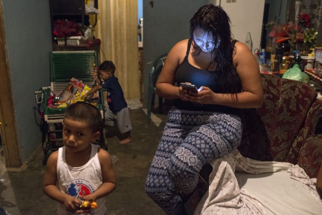 Greicy смотрит на свой мобильный телефон, пока ее сын и ее племянник играют