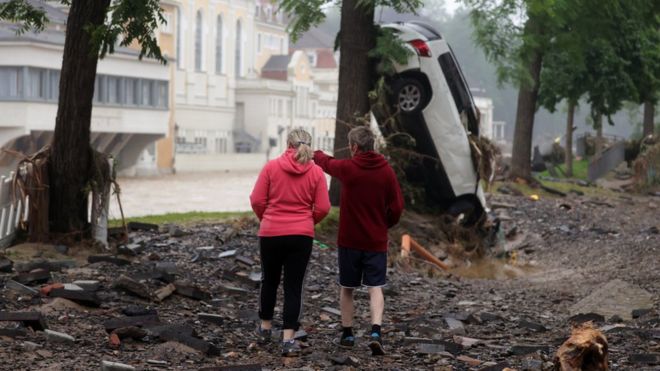 Two persons stand amid the debris near a damaged car and trees after flooding in Bad Neuenahr-Ahrweiler