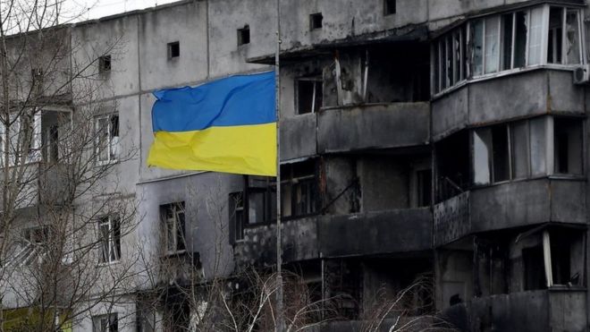 The Ukraine flag flies in front of a burned out building
