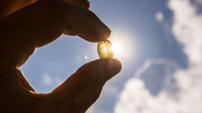 Pessoa segura comprimido de vitamina D na contraluz do Sol