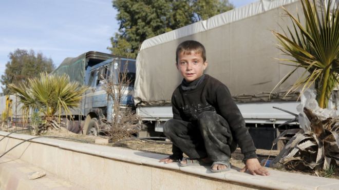 A boy plays near aid convoys in a rebel-held Syrian town