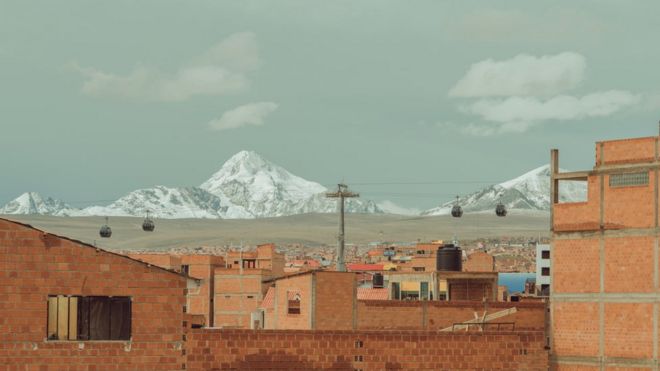 Casas com tijolo aparente e sem pintura e, em segundo plano, as cordilheiras dos Andes com gelo