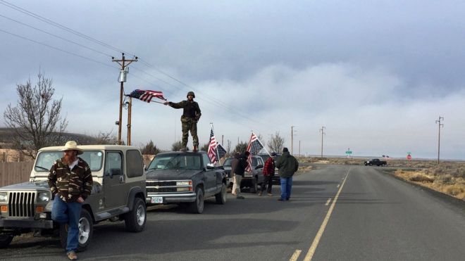 Люди машут американскими флагами возле убежища Малхеур