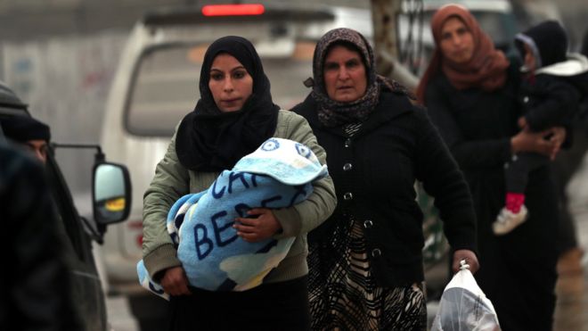 Сирийские женщины несут детей и сумки в контролируемом курдами северном сирийском городе Манбидж 30 декабря 2018 года